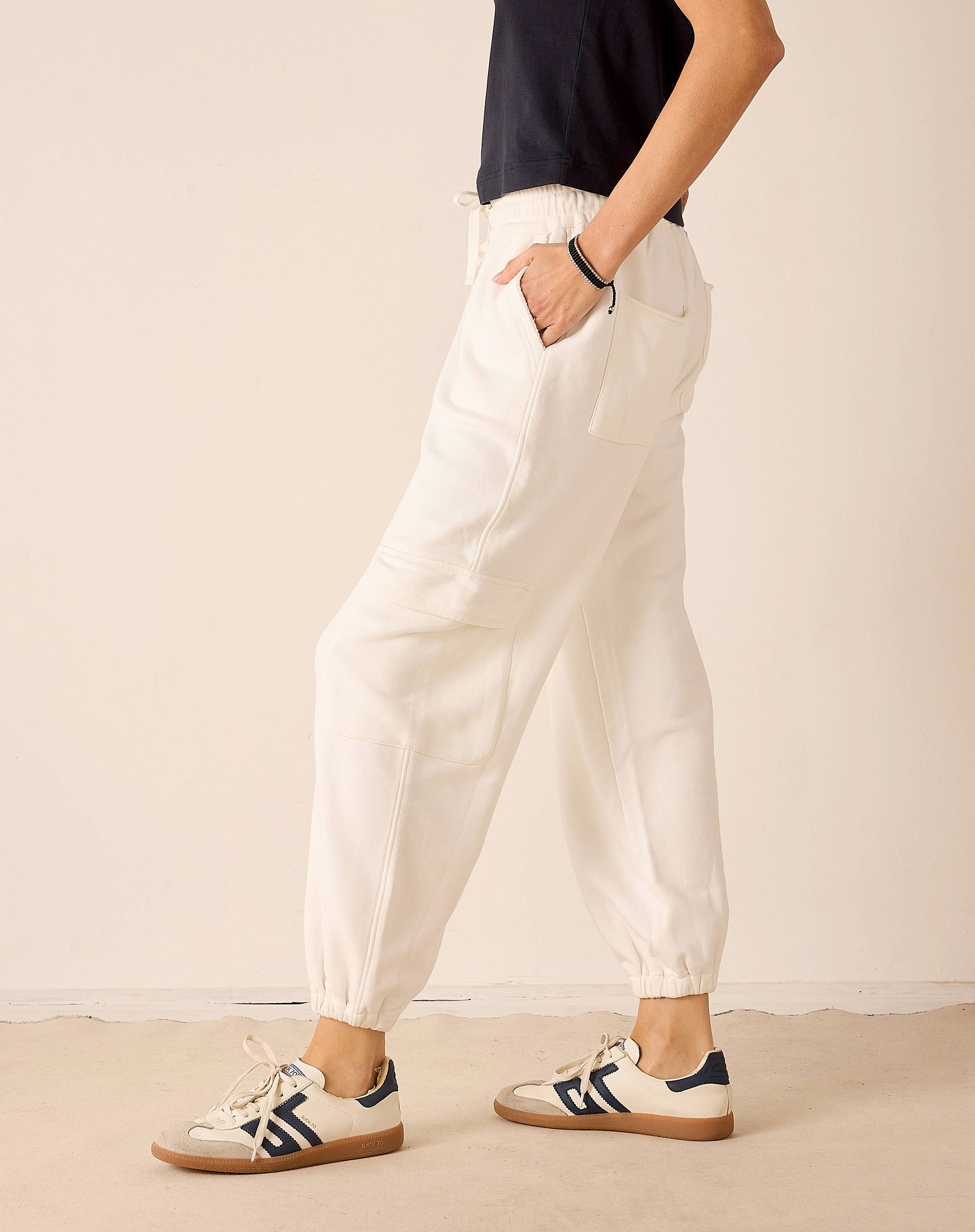 Person wearing white pants and black and white sneakers on a beige background