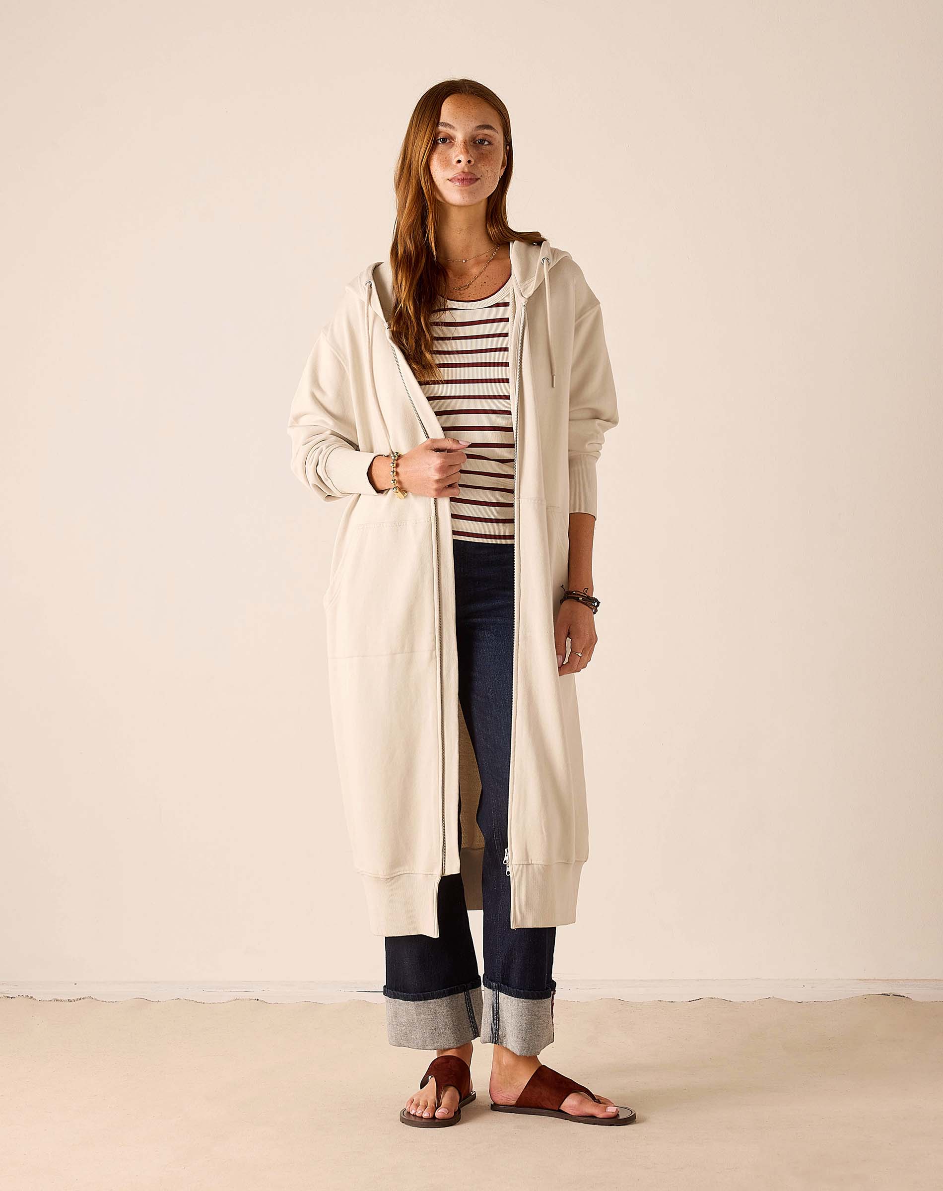 Bone hoodie featuring a longer length and hood, worn over a striped top and jeans.