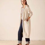 Bone hoodie with a hood and front pocket over a striped tee and dark trousers.