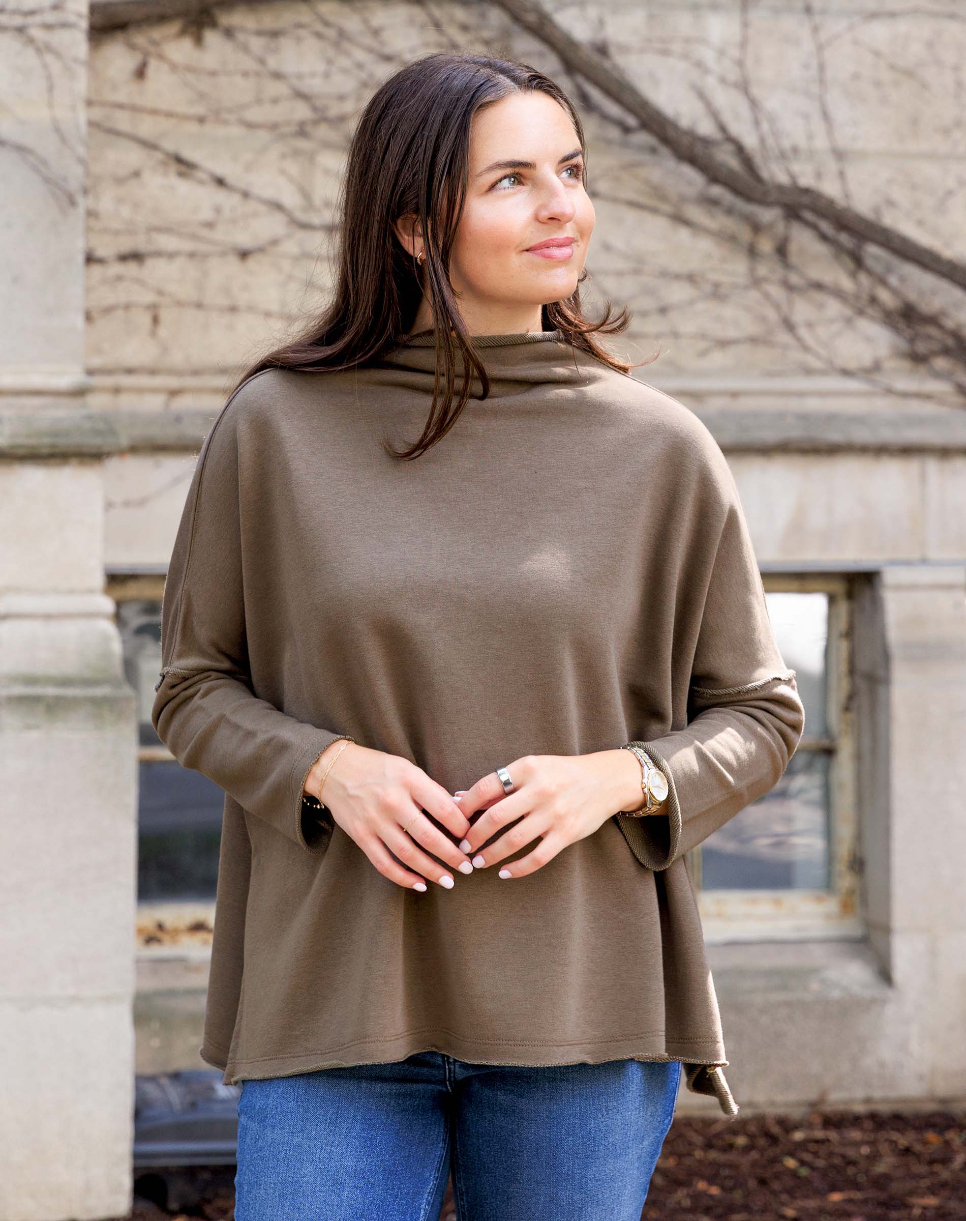 Woman wearing a brown turtleneck sweater and blue jeans standing outdoors.