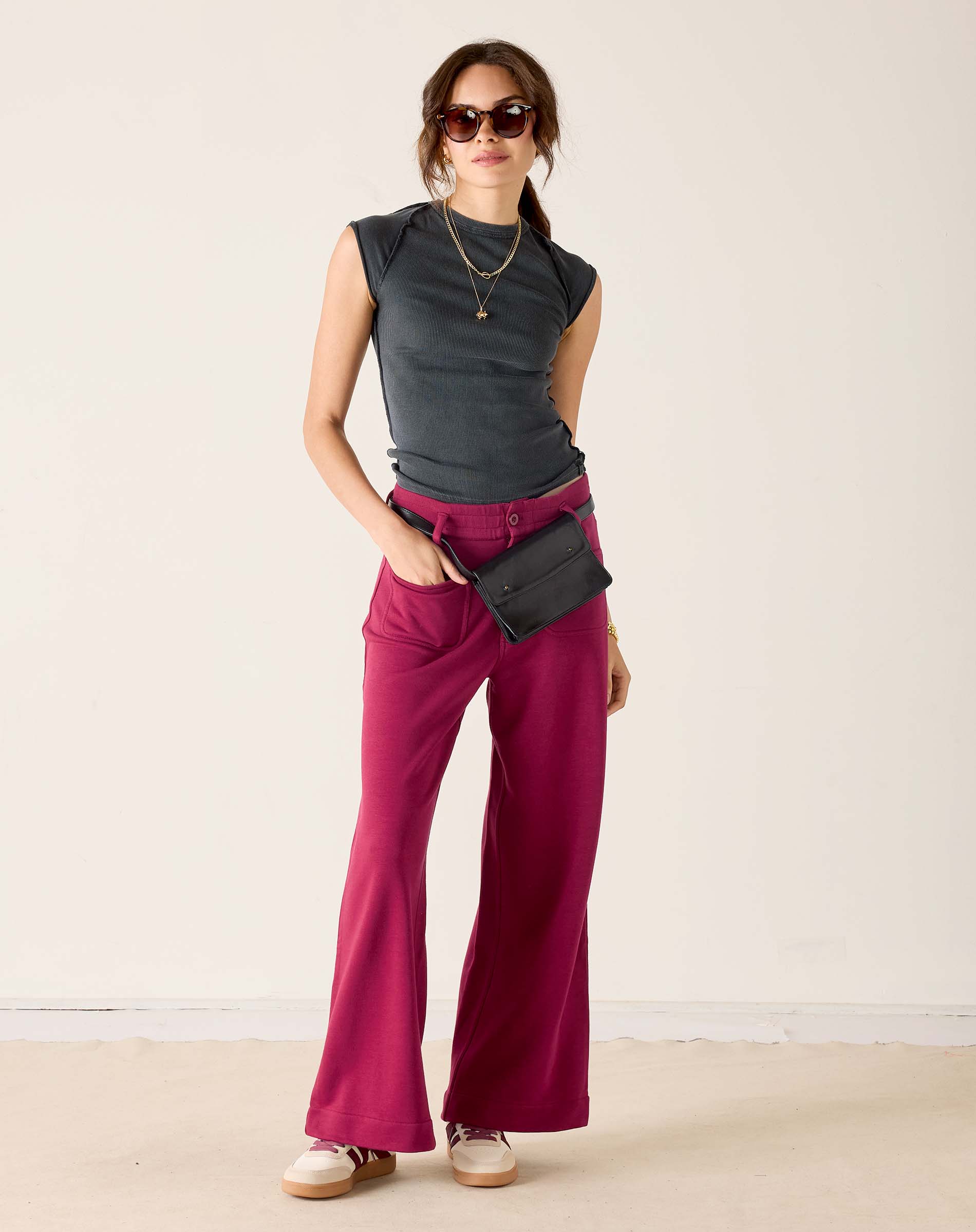 Woman wearing a gray sleeveless top and pink pants with a black belt and bag on a white background