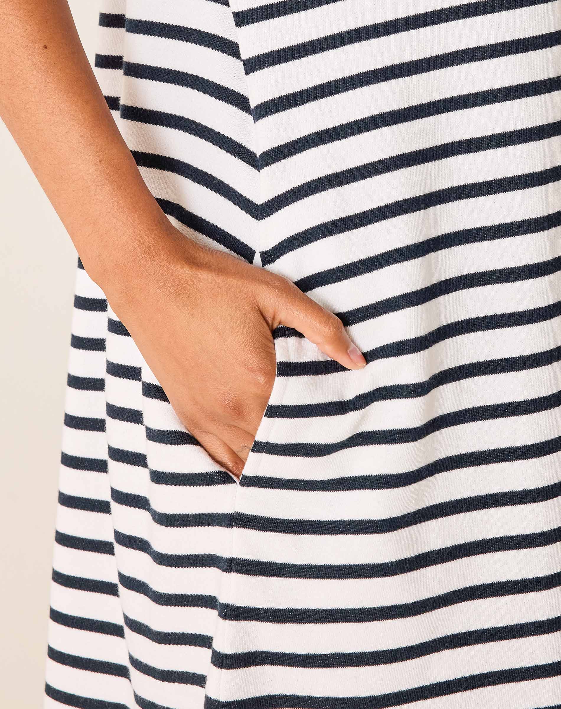 Close-up of a person wearing a white dress with navy blue stripes, holding their hand in a pocket.