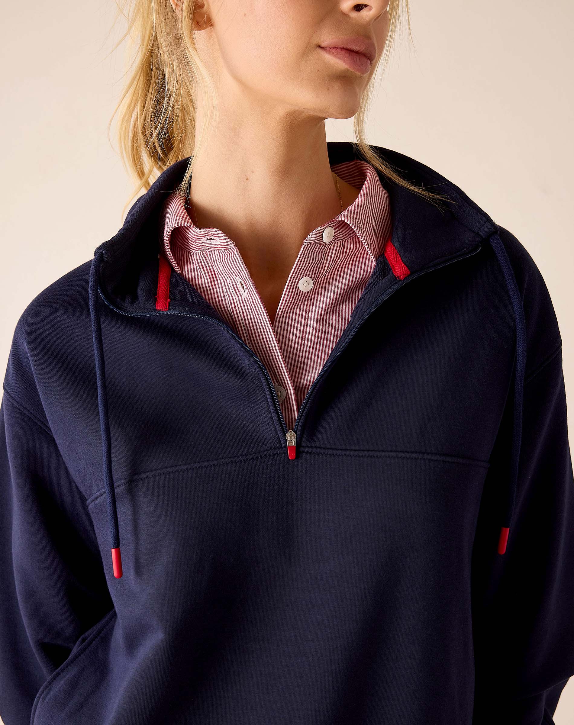 Cadet blue quarter-zip sweatshirt with red drawstring details and a striped button-down shirt underneath.