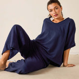 Woman wearing a navy blue outfit sitting on a beige surface with a plain background