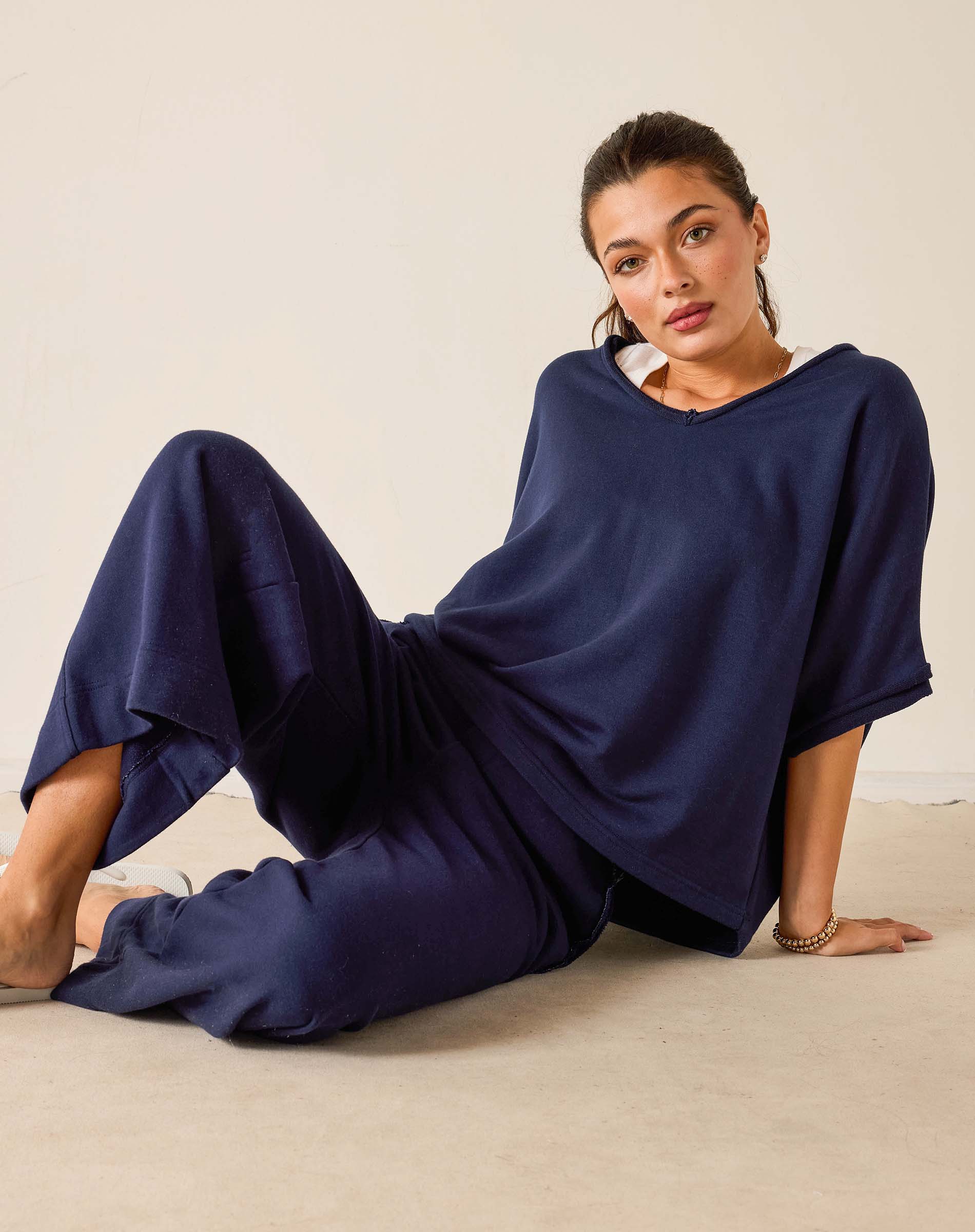 Woman wearing a navy blue outfit sitting on a beige surface with a plain background