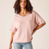 Woman wearing a pink oversized top and light blue jeans on a beige background