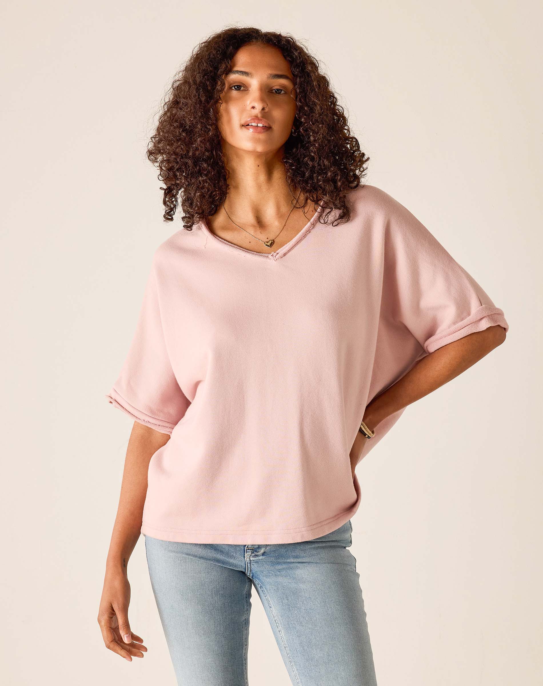 Woman wearing a pink oversized top and light blue jeans on a beige background