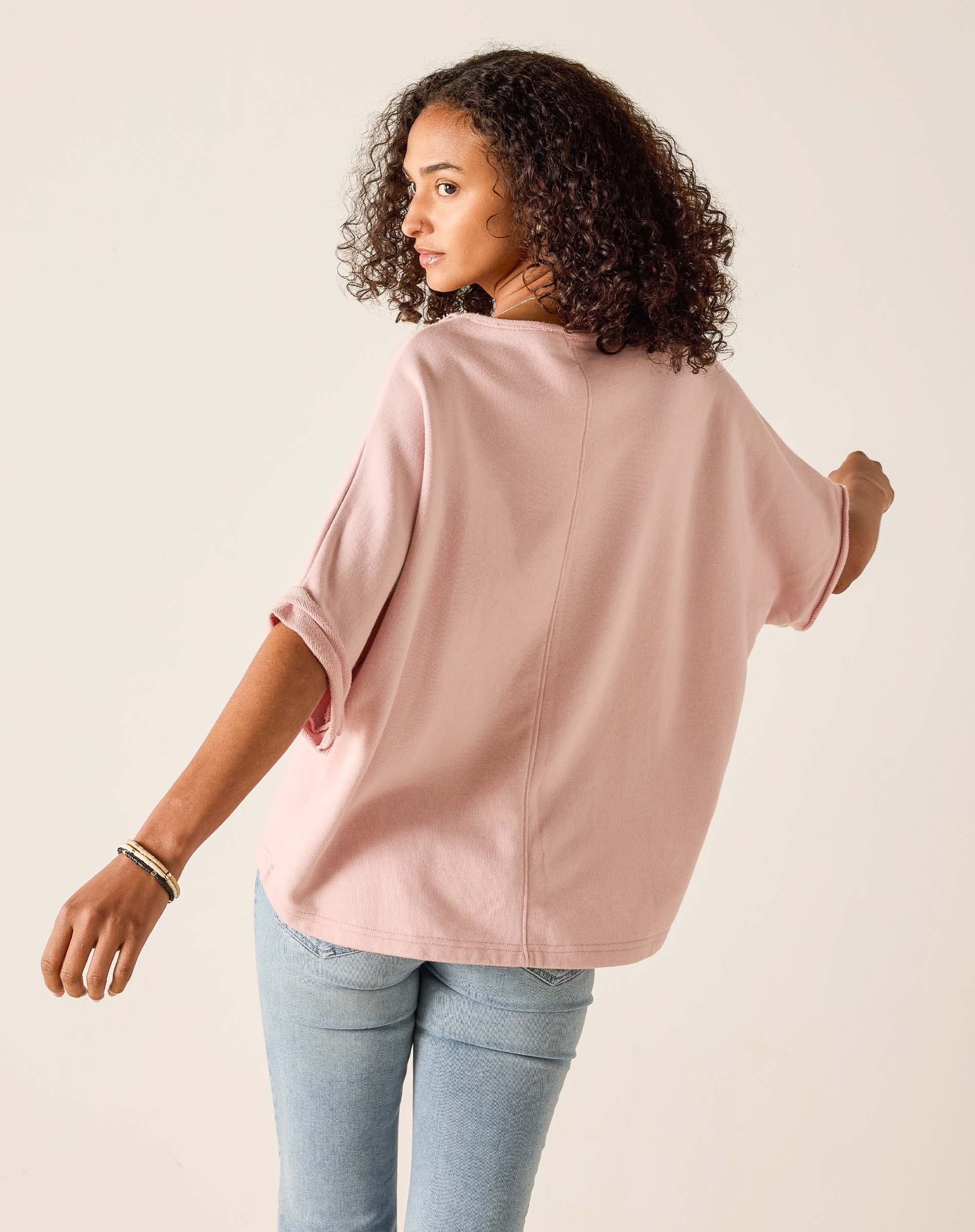 Woman wearing a light pink oversized shirt and light blue jeans on a beige background