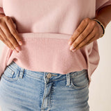 Person wearing a pink sweater and blue jeans with a neutral background