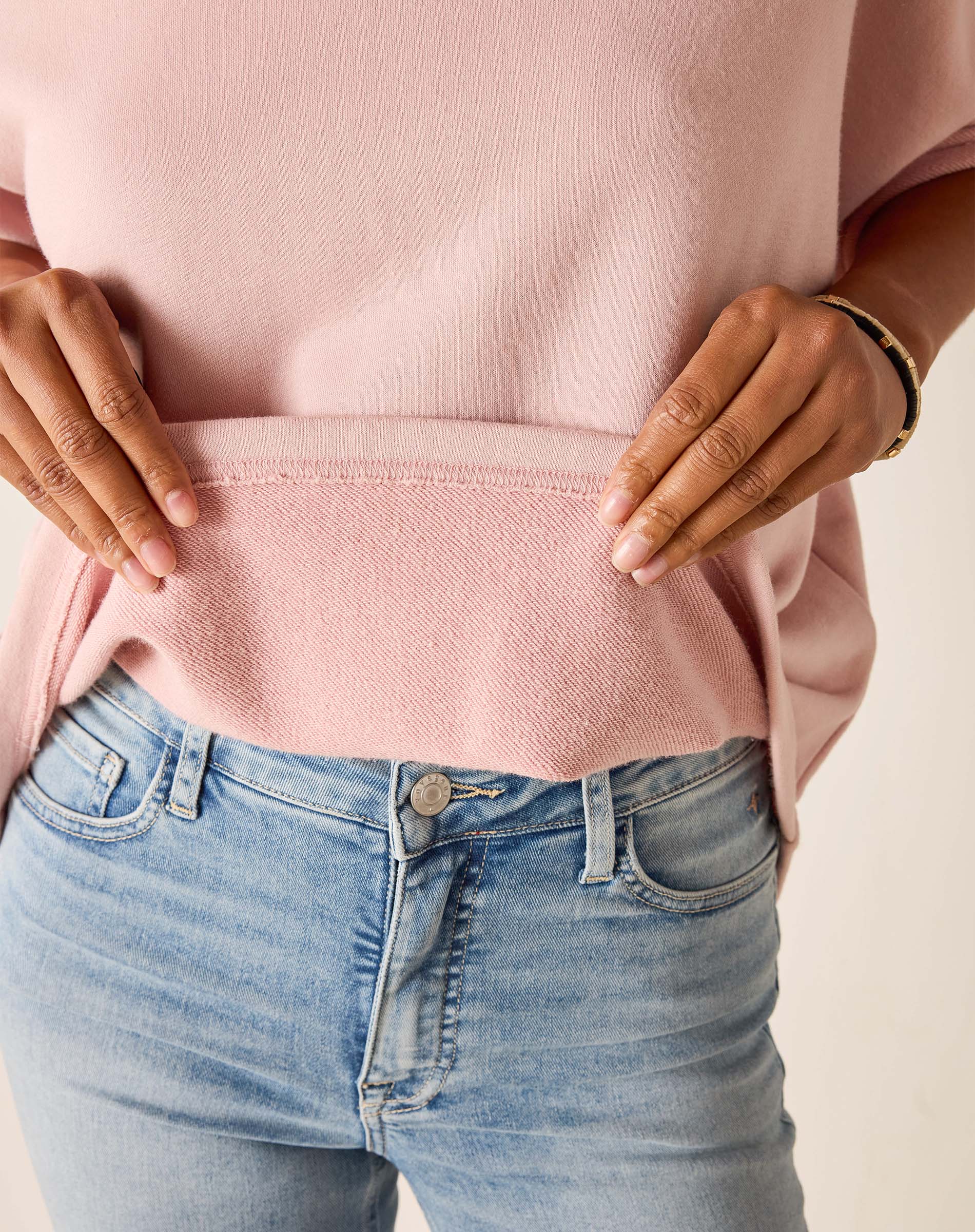 Person wearing a pink sweater and blue jeans with a neutral background