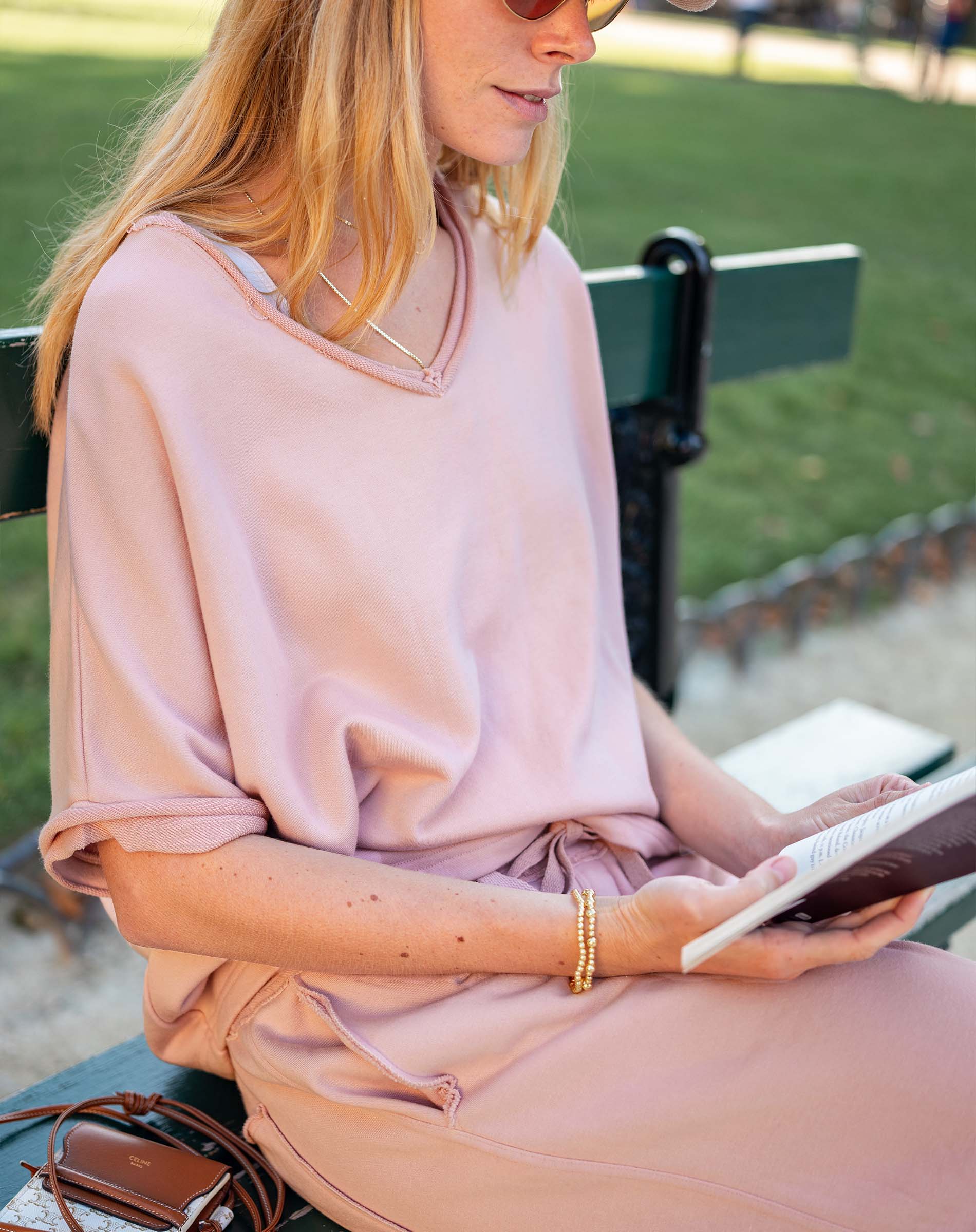 Woman in a pink dress sitting on a bench reading a book outdoors.
