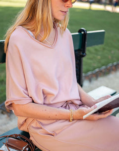 Woman in a pink dress sitting on a bench reading a book outdoors.