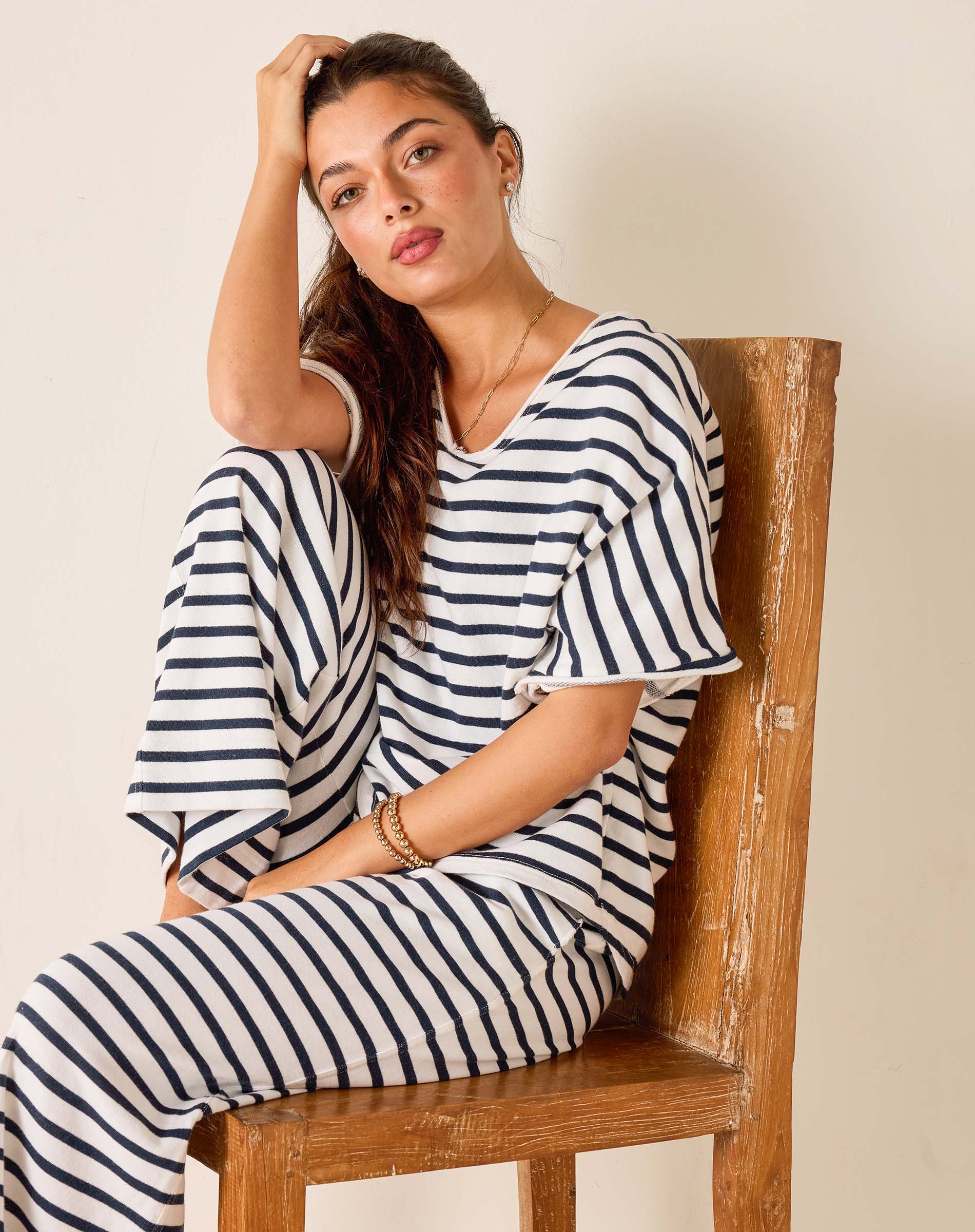 Woman wearing a black and white striped outfit sitting on a wooden chair.