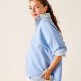 Woman wearing a light blue poncho with striped trim on a beige background