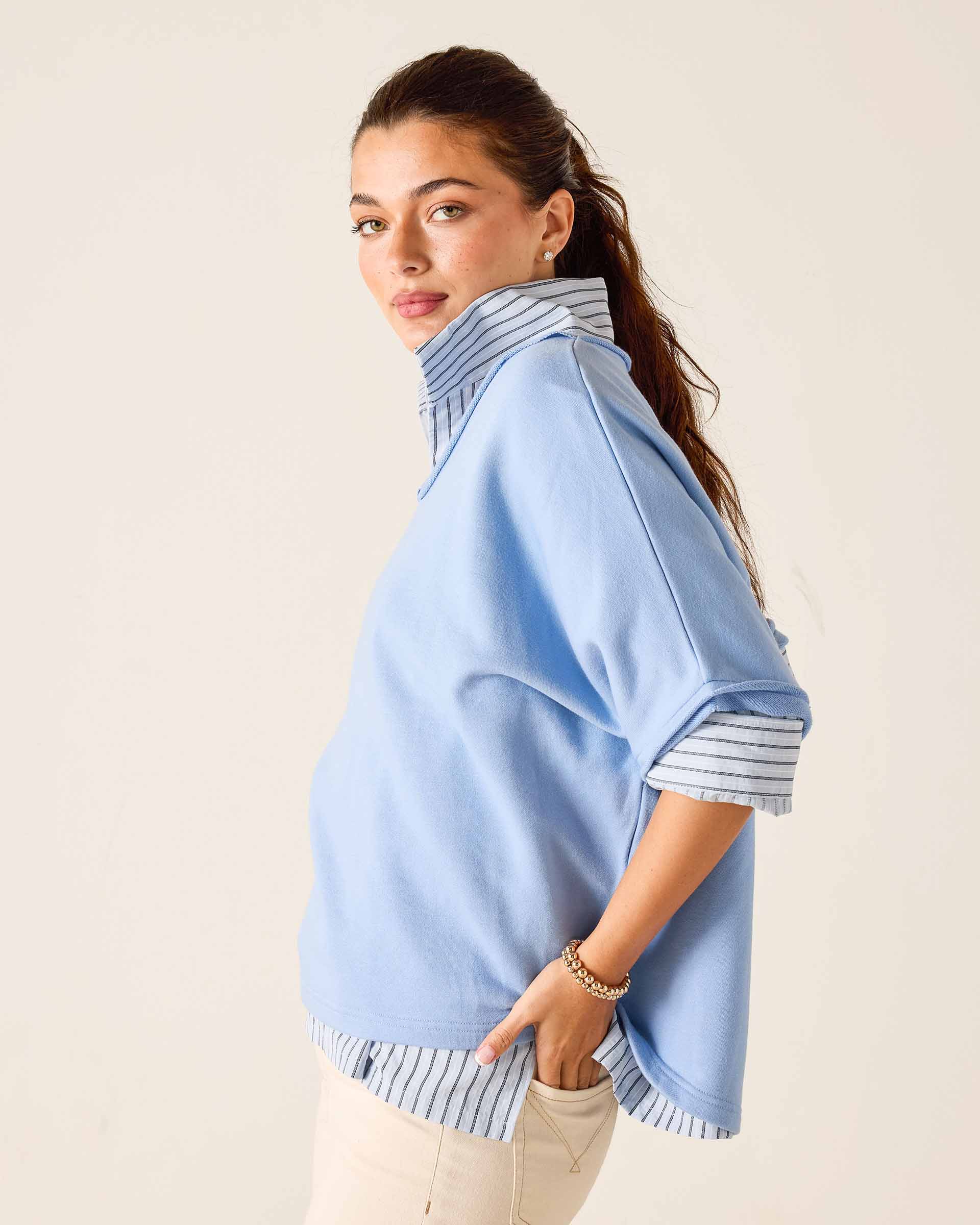 Woman wearing a light blue poncho with striped trim on a beige background