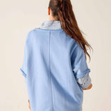 Person wearing a light blue denim jacket with striped cuffs on a beige background