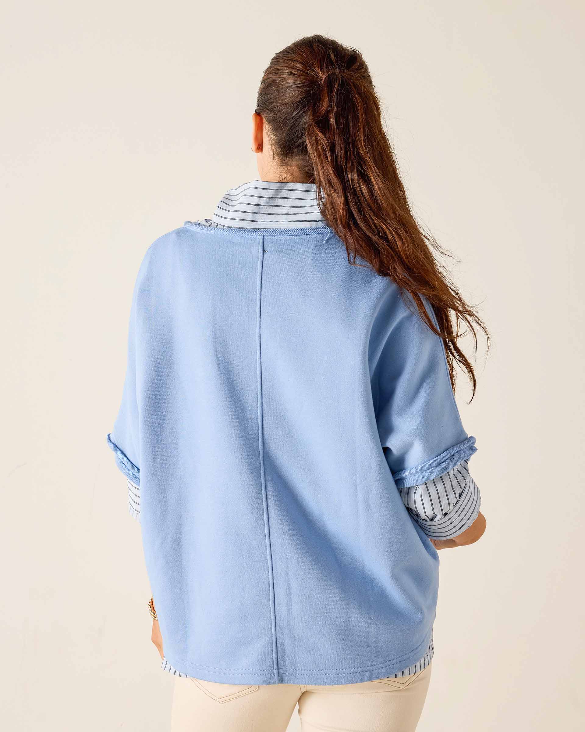 Person wearing a light blue denim jacket with striped cuffs on a beige background
