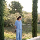Woman in a light blue outfit standing by a pool with greenery in the background