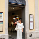 Woman in a white outfit standing in front of a station entrance with 'Accès à la gare' sign.