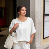 Woman in white outfit holding a tote bag, standing against a building wall.