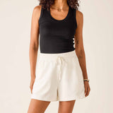 Woman wearing a black tank top and white shorts on a beige background