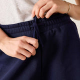 Person adjusting navy blue pants with a neutral background
