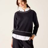 Woman wearing a black sweater with white trim on a beige background