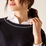 Woman wearing a black sweater with white trim and a white shirt underneath, against a neutral background.