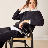 Person sitting on a chair wearing a black and white outfit against a plain background