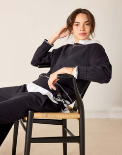 Person sitting on a chair wearing a black and white outfit against a plain background