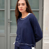 Woman wearing a navy blue outfit with white trim standing in front of a gray door.