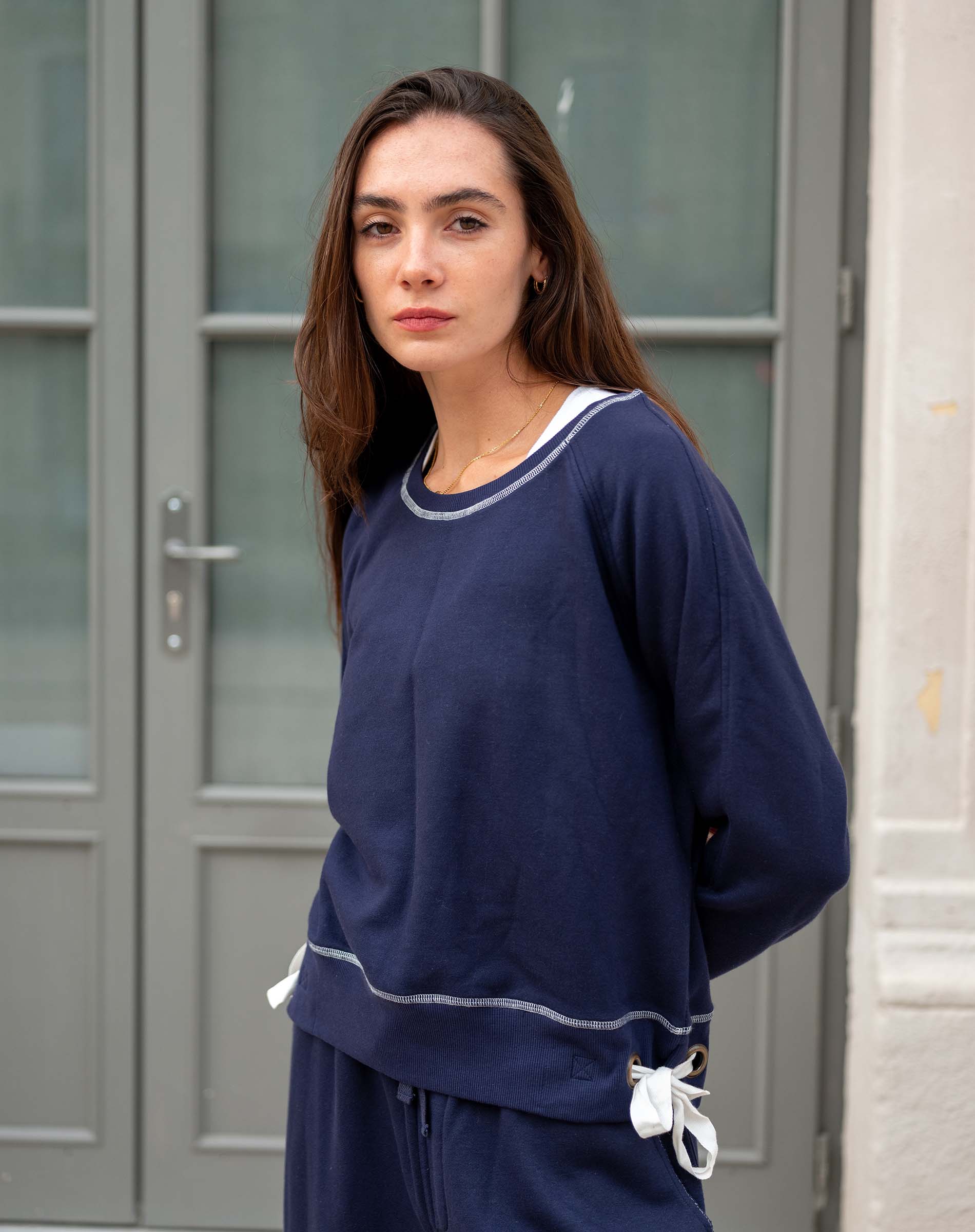 Woman wearing a navy blue outfit with white trim standing in front of a gray door.