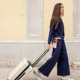 Woman in navy outfit pulling a white suitcase on a street.