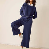 Woman wearing a navy blue tracksuit with white sneakers on a beige background