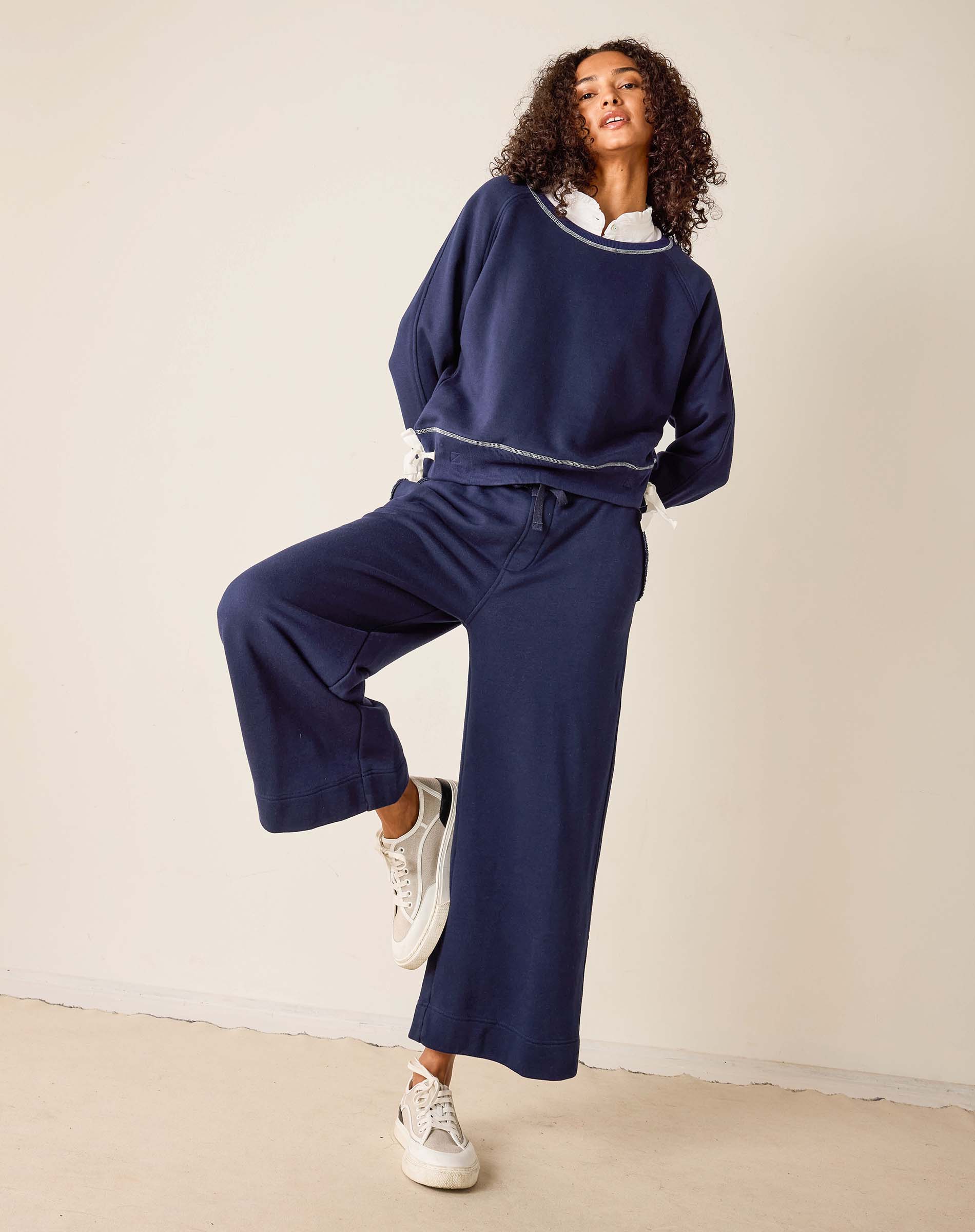Woman wearing a navy blue tracksuit with white sneakers on a beige background