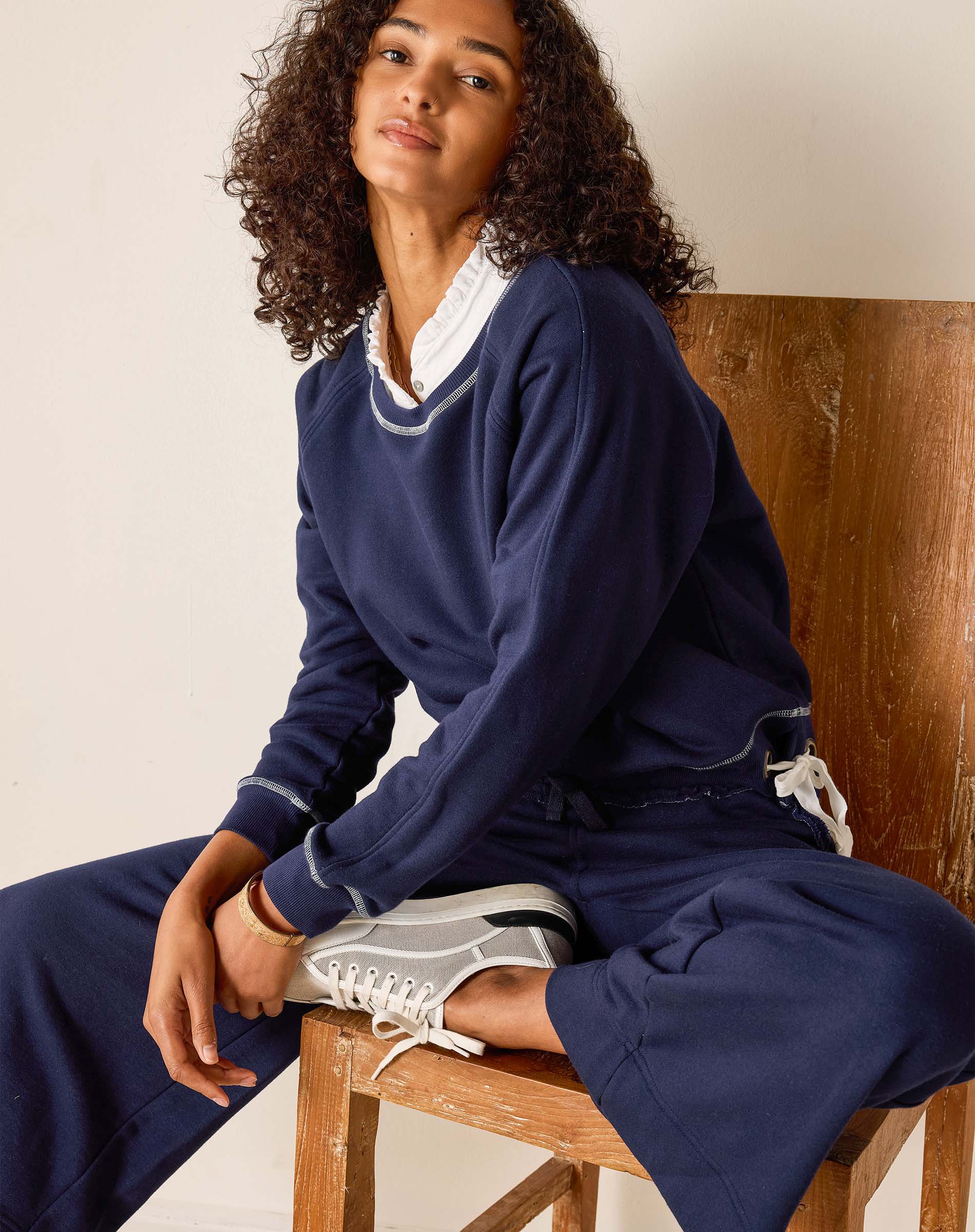 Person wearing a navy blue outfit sitting on a wooden chair.