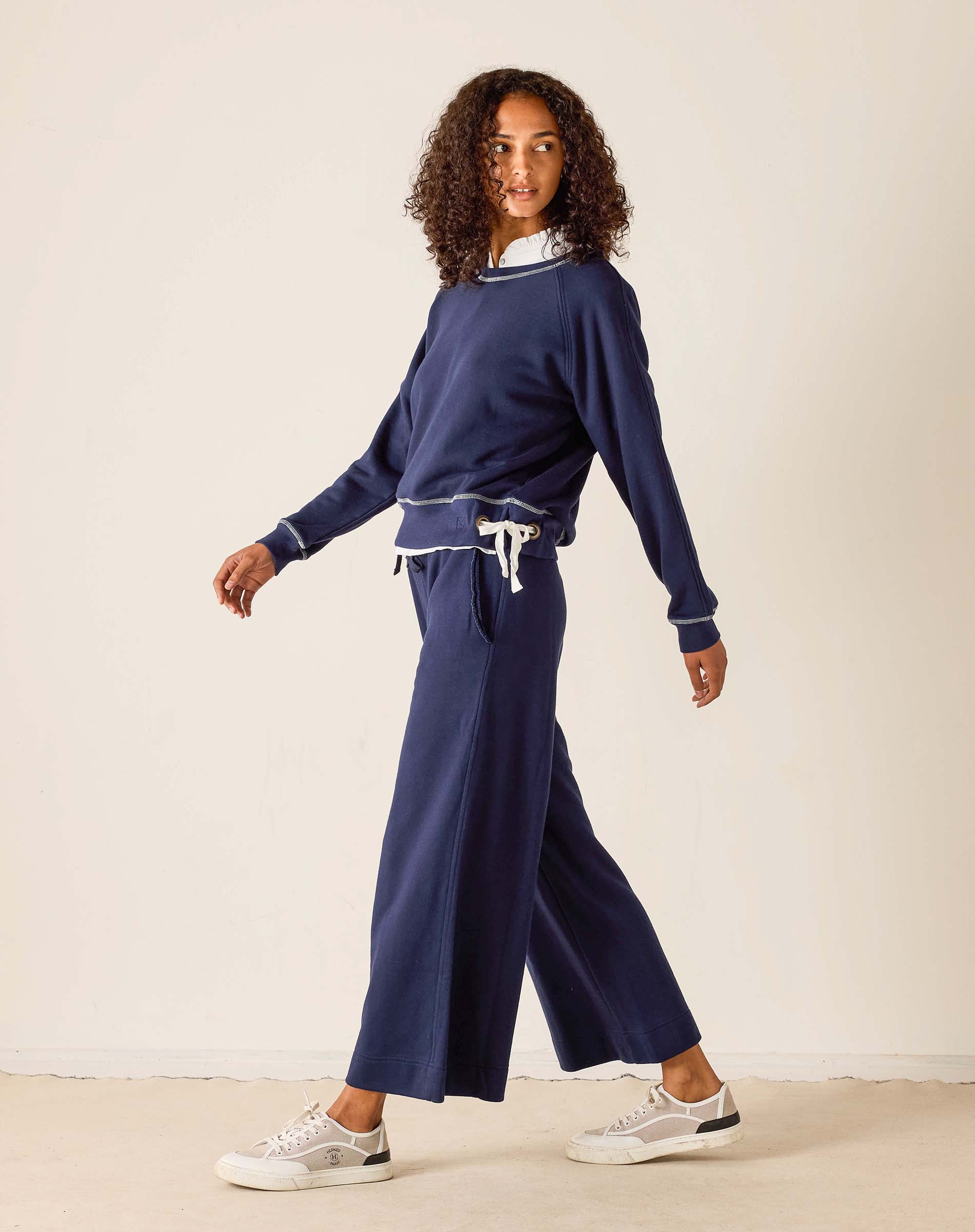 Woman wearing a navy blue outfit with white sneakers on a plain background