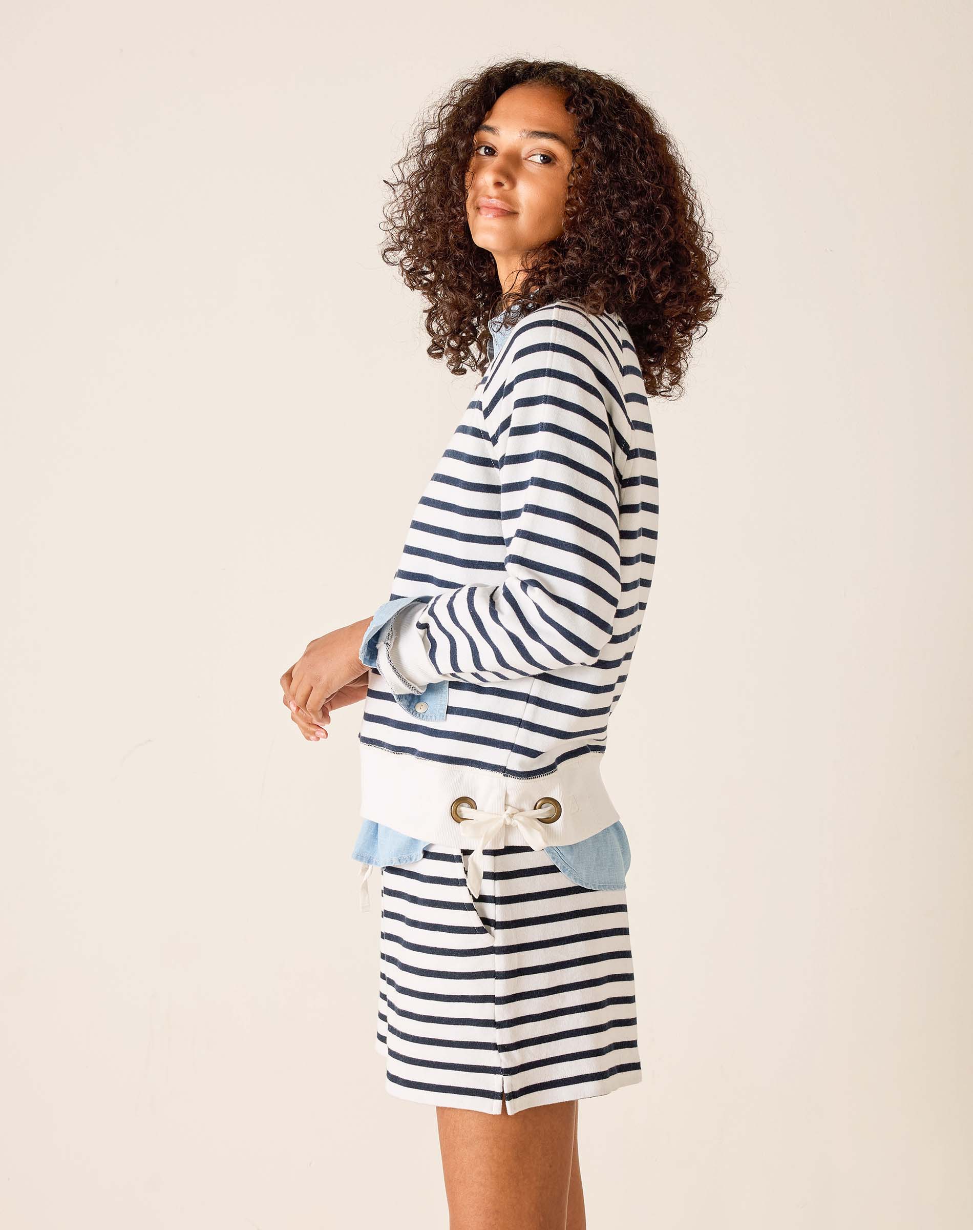 Woman wearing a striped sweater and denim skirt on a plain background