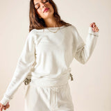 Woman wearing a white sweatshirt and pants against a plain background