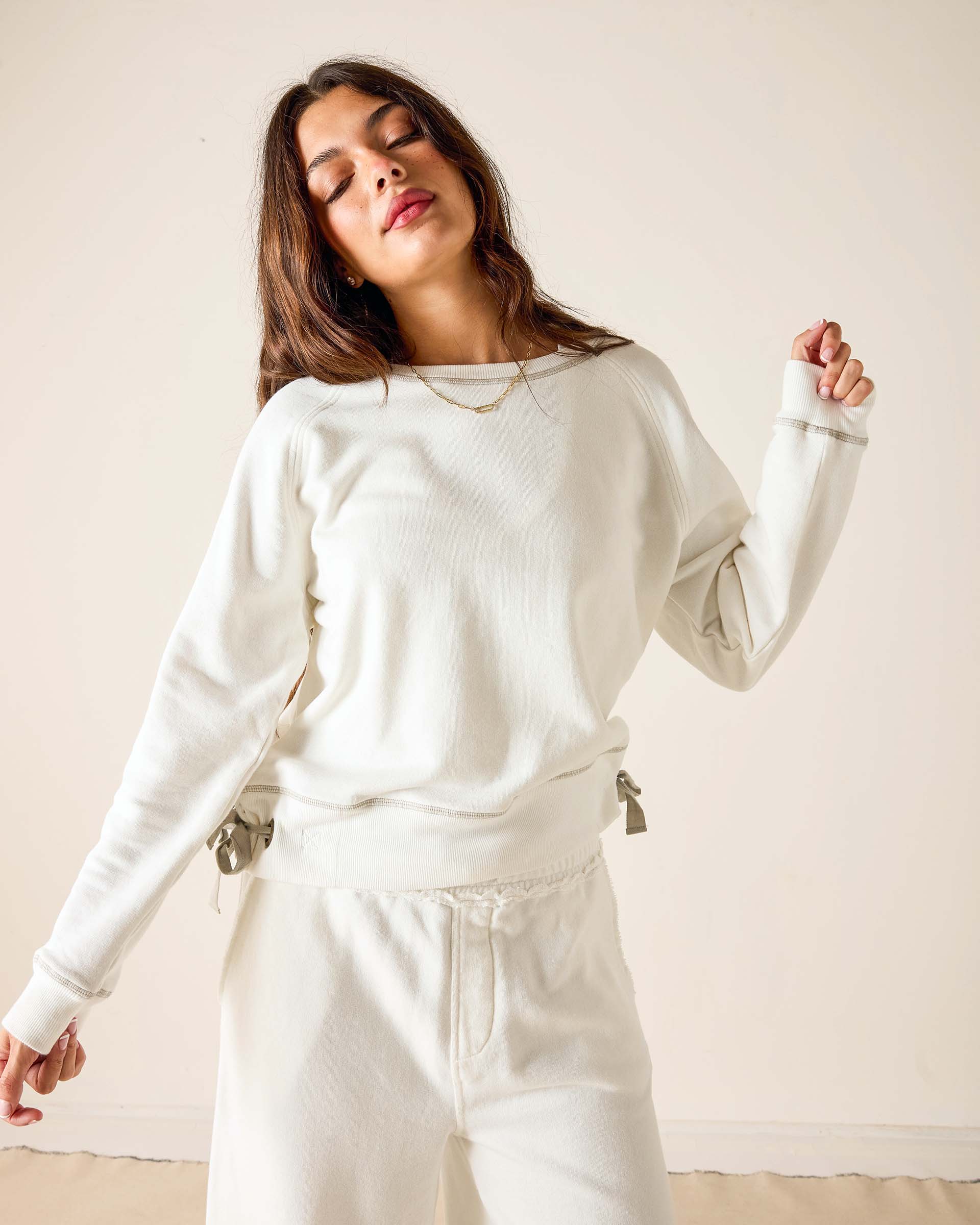 Woman wearing a white sweatshirt and pants against a plain background
