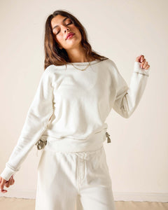 Woman wearing a white sweatshirt and pants against a plain background