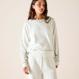Woman wearing a light gray sweatshirt and pants against a beige background