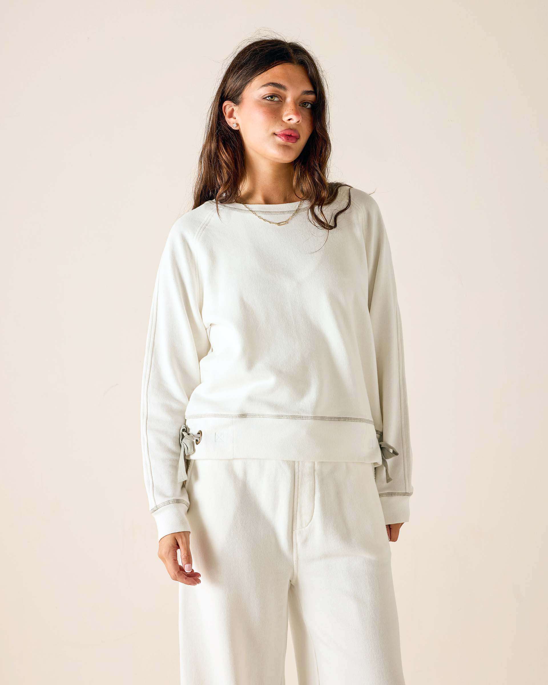 Woman wearing a light gray sweatshirt and pants against a beige background