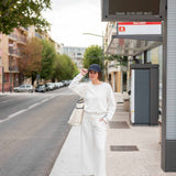Person standing at a bus stop wearing a white outfit with a black cap.