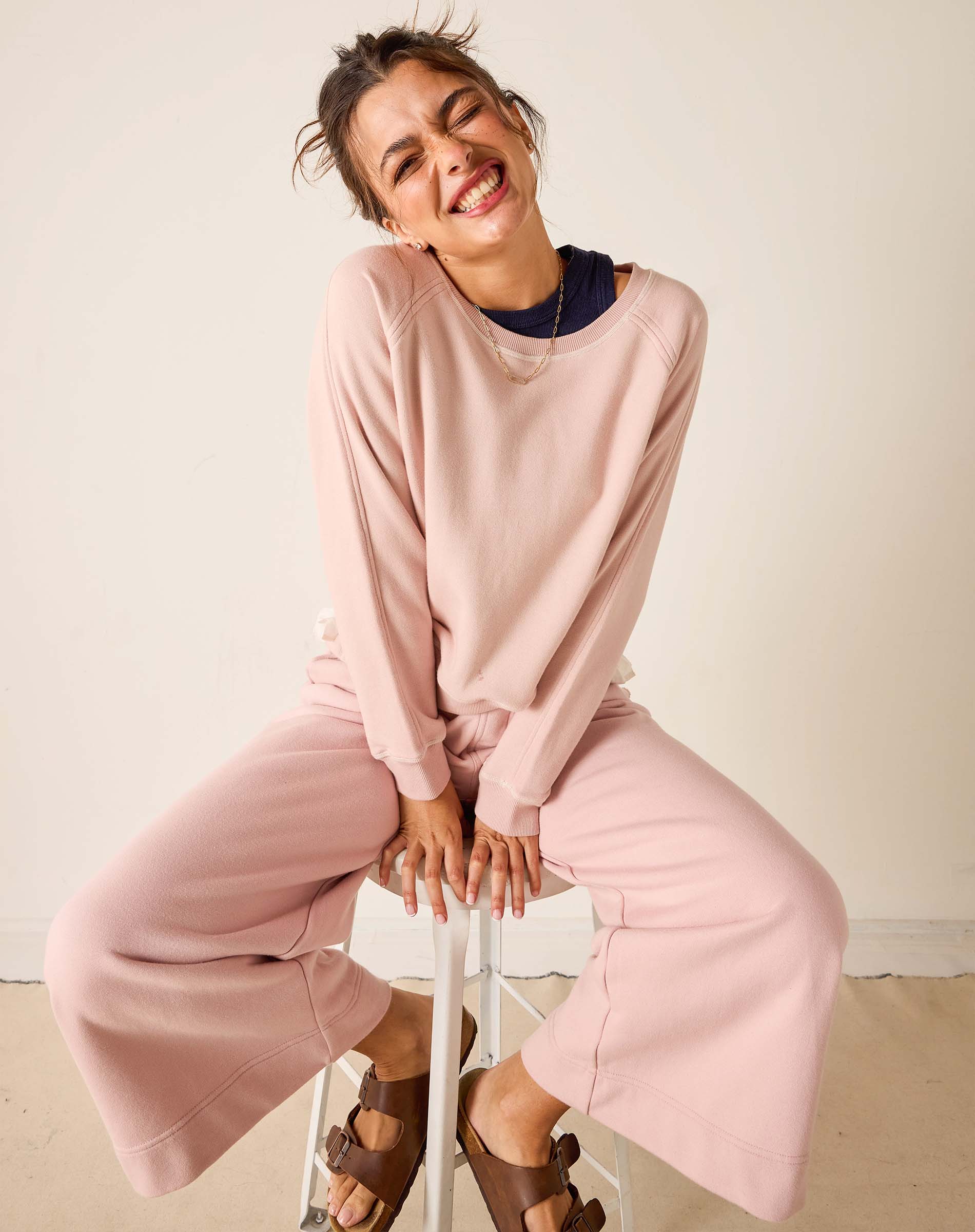 Woman sitting on a stool wearing a pink outfit against a plain background