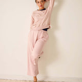 Woman wearing a pink sweatshirt and pants against a white wall.