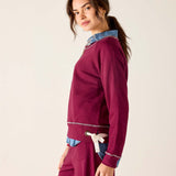 Woman wearing a burgundy outfit with denim accents on a plain background