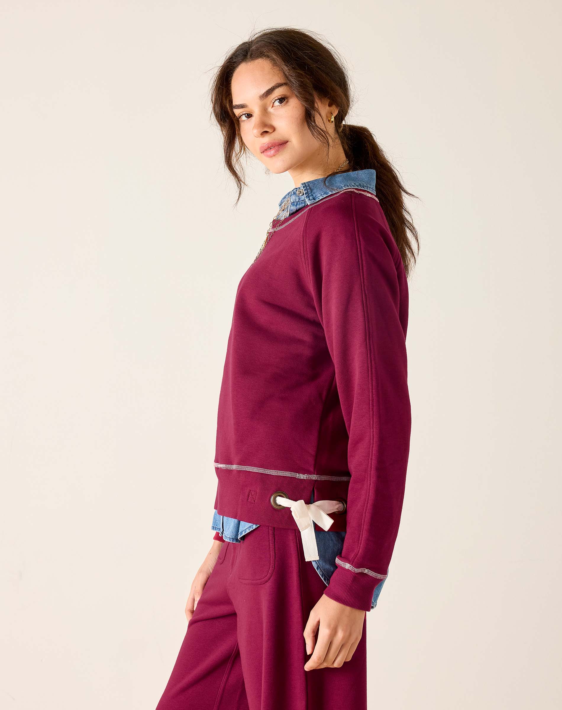 Woman wearing a burgundy outfit with denim accents on a plain background