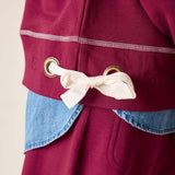 Close-up of a maroon jacket with a white bow and gold buttons on a beige background