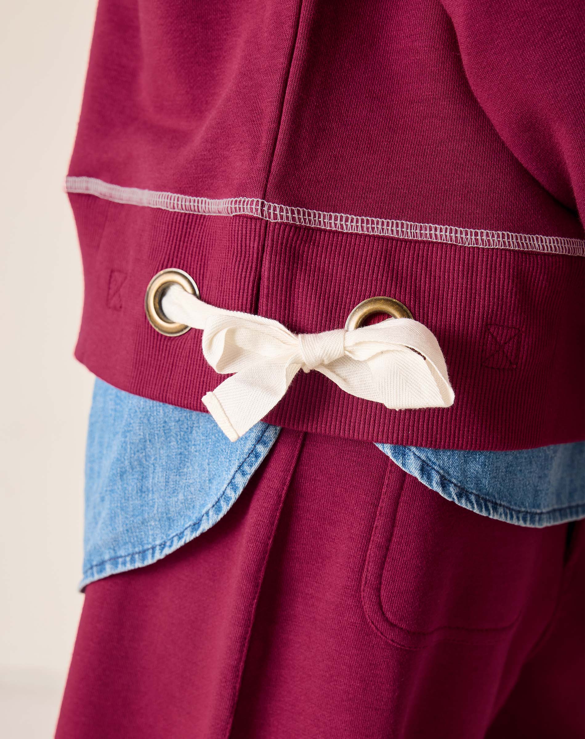 Close-up of a maroon jacket with a white bow and gold buttons on a beige background